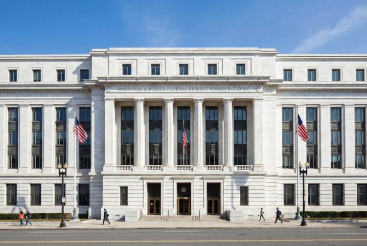 Vista frontal y simétrica de la fachada estilo Beaux-Arts del edificio de la Reserva Federal en Washington D.C. La imagen destaca la solidez del mármol blanco y las columnas clásicas bajo luz natural, simbolizando la autoridad central del banco central de EE.UU.