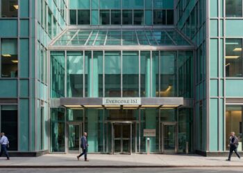 Fotografía de la entrada principal del edificio de oficinas de Evercore ISI en Nueva York, caracterizada por su moderna fachada de vidrio verde. Un cartel prominente sobre las puertas giratorias muestra claramente el nombre "EVERCORE ISI". Varios peatones caminan por la acera frente al edificio bajo la luz del día.