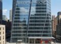Fotografía de la Torre Bank of America en Nueva York, mostrando la fachada de cristal facetado con el gran letrero y logotipo de "BANK OF AMERICA" integrados en la parte superior. Una sucursal del banco es visible a nivel de calle.