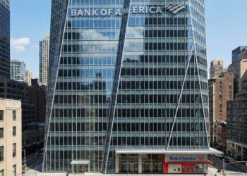 Fotografía de la Torre Bank of America en Nueva York, mostrando la fachada de cristal facetado con el gran letrero y logotipo de "BANK OF AMERICA" integrados en la parte superior. Una sucursal del banco es visible a nivel de calle.