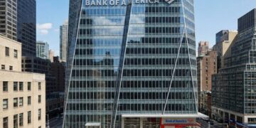 Fotografía de la Torre Bank of America en Nueva York, mostrando la fachada de cristal facetado con el gran letrero y logotipo de "BANK OF AMERICA" integrados en la parte superior. Una sucursal del banco es visible a nivel de calle.