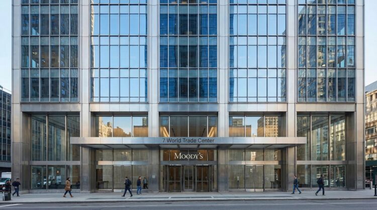Vista frontal a nivel de calle de la entrada moderna de cristal y acero del edificio 7 World Trade Center. Los letreros "7 World Trade Center" y el logotipo "MOODY'S" son visibles sobre las puertas giratorias mientras peatones caminan por la acera.
