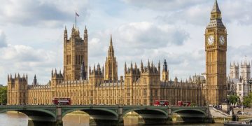 Fotografía diurna del Palacio de Westminster y la Torre Elizabeth (Big Ben) a través del río Támesis, con el puente de Westminster y un cielo parcialmente nublado.