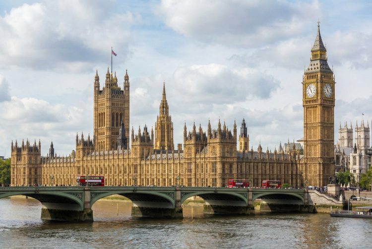 Fotografía diurna del Palacio de Westminster y la Torre Elizabeth (Big Ben) a través del río Támesis, con el puente de Westminster y un cielo parcialmente nublado.