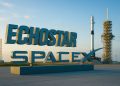 Logos de EchoStar y Space X en gran formato frente a una plataforma de lanzamiento iluminada.