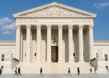 Fotografía arquitectónica frontal y simétrica del edificio de mármol blanco de la Corte Suprema de los Estados Unidos bajo un cielo azul con nubes. El frontón sobre las columnas corintias muestra la inscripción "EQUAL JUSTICE UNDER LAW". Varias personas caminan por la amplia plaza y las escaleras frente al edificio.