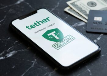 Fotografía de primer plano de un teléfono inteligente moderno sobre una superficie de mármol negro. La pantalla del teléfono muestra la aplicación Tether con el logotipo verde, el saldo en USAT y un sello verde que dice "FEDERALLY REGULATED". En segundo plano, se ven billetes de cien dólares estadounidenses y una tarjeta de crédito negra desenfocados.