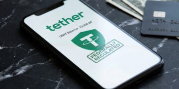 Fotografía de primer plano de un teléfono inteligente moderno sobre una superficie de mármol negro. La pantalla del teléfono muestra la aplicación Tether con el logotipo verde, el saldo en USAT y un sello verde que dice "FEDERALLY REGULATED". En segundo plano, se ven billetes de cien dólares estadounidenses y una tarjeta de crédito negra desenfocados.