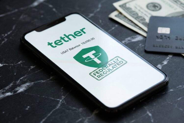 Fotografía de primer plano de un teléfono inteligente moderno sobre una superficie de mármol negro. La pantalla del teléfono muestra la aplicación Tether con el logotipo verde, el saldo en USAT y un sello verde que dice "FEDERALLY REGULATED". En segundo plano, se ven billetes de cien dólares estadounidenses y una tarjeta de crédito negra desenfocados.