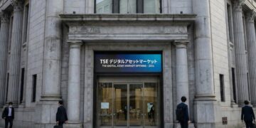 Fotografía exterior a nivel de calle de la entrada principal del edificio clásico de piedra de la Bolsa de Tokio (TSE). Sobre las puertas de vidrio, una gran pantalla digital azul muestra el texto bilingüe: "TSE デジタルアセットマーケット" y "TSE DIGITAL ASSET MARKET OPENING - 2026". Varios peatones con traje de negocios caminan por la acera frente a la institución financiera.