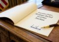 Fotografía de primer plano sobre un escritorio de madera tallada estilo Resolute, mostrando una orden ejecutiva abierta con el encabezado "Executive Order: Mortgage-Backed Securities Purchase" y una firma manuscrita en tinta azul. Una pluma estilográfica descansa sobre el documento.