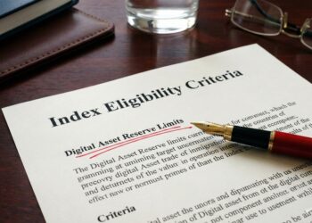 Fotografía de primer plano sobre un escritorio de madera oscura que muestra un documento formal con el título "Index Eligibility Criteria". Una pluma estilográfica roja apunta directamente a una cláusula específica que ha sido subrayada vigorosamente en tinta roja: "Digital Asset Reserve Limits". Al lado hay unas gafas de lectura y un vaso de agua, sugiriendo un entorno de revisión corporativa.