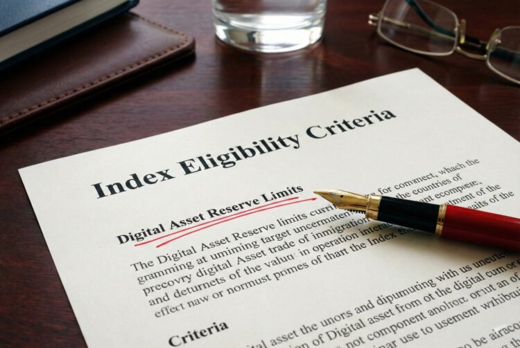 Fotografía de primer plano sobre un escritorio de madera oscura que muestra un documento formal con el título "Index Eligibility Criteria". Una pluma estilográfica roja apunta directamente a una cláusula específica que ha sido subrayada vigorosamente en tinta roja: "Digital Asset Reserve Limits". Al lado hay unas gafas de lectura y un vaso de agua, sugiriendo un entorno de revisión corporativa.