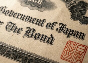 Fotografía macro de un documento de papel envejecido y texturizado que muestra el texto "Government of Japan" y "The Bond" en una tipografía negra ornamentada. Un sello oficial rojo cuadrado con caracteres japoneses es visible en la esquina inferior derecha, rodeado de patrones de grabado detallados.