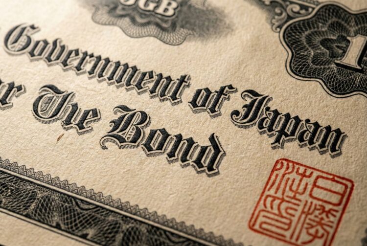 Fotografía macro de un documento de papel envejecido y texturizado que muestra el texto "Government of Japan" y "The Bond" en una tipografía negra ornamentada. Un sello oficial rojo cuadrado con caracteres japoneses es visible en la esquina inferior derecha, rodeado de patrones de grabado detallados.