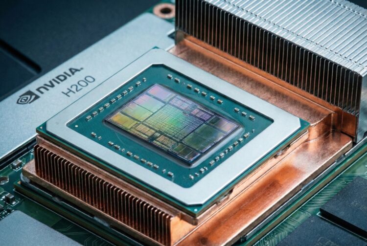 Una fotografía de primer plano muestra el módulo del procesador gráfico NVIDIA H200. El chip de silicio central, con su intrincada estructura de circuitos visible en tonos verdes, dorados y azules, está montado sobre un sustrato verde rodeado de pequeños condensadores. Un marco metálico con el logotipo "NVIDIA H200" grabado rodea el chip. Todo el conjunto está montado sobre una base de disipador de calor de cobre grande, con aletas de enfriamiento de aluminio plateado visibles en la parte superior y posterior. La iluminación resalta las texturas metálicas y del silicio.