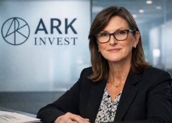 Cathie Wood en oficina corporativa con logo de ARK Invest al fondo.