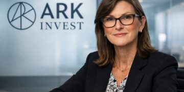 Cathie Wood en oficina corporativa con logo de ARK Invest al fondo.