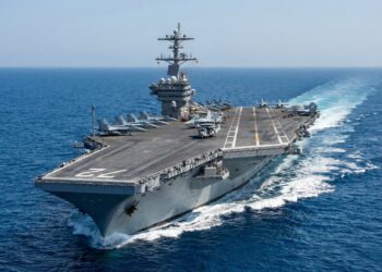 Vista aérea del portaaviones de la Armada de EE. UU., USS Abraham Lincoln (CVN-72), navegando en aguas azules abiertas con su cubierta de vuelo llena de aviones de combate y aviones de alerta temprana. El número '72' es visible en la proa mientras el buque deja una estela blanca bajo un cielo despejado.