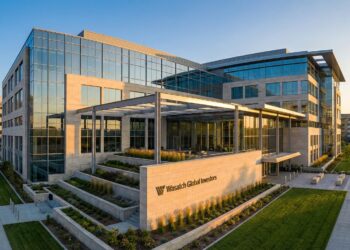Una imagen panorámica exterior del moderno edificio de oficinas de Wasatch Global Investors, construido con vidrio y piedra de color claro, y bañado por la luz dorada del atardecer. El letrero de la empresa es visible en una pared de piedra en primer plano, junto a jardines en terrazas y pasarelas de hormigón.