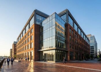 Fotografía arquitectónica panorámica de la sede de Circle Internet Financial en el distrito de Seaport, Boston. El edificio combina fachadas de ladrillo histórico con una adición moderna de vidrio y acero. El logo de Circle está montado en la entrada de vidrio. La luz dorada de la mañana ilumina la escena mientras personas caminan por el paseo marítimo de ladrillo junto a un puerto deportivo.