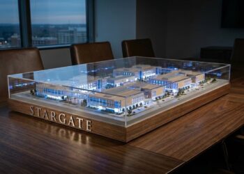 Un modelo arquitectónico a escala detallado e iluminado del complejo de edificios "STARGATE" se encuentra bajo una cubierta de acrílico transparente sobre una gran mesa de conferencias de madera. Las letras metálicas "STARGATE" son visibles en la base del modelo. De fondo, se ve una vista de la ciudad al atardecer a través de una ventana.