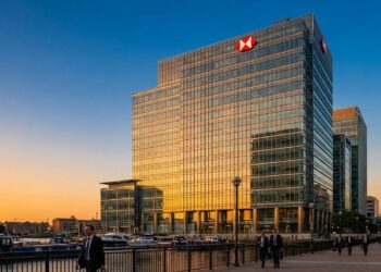 Fotografía exterior del rascacielos de la sede de HSBC (8 Canada Square) en los Docklands de Londres durante la puesta de sol. La fachada de vidrio del edificio refleja intensamente la luz cálida y dorada del sol. Profesionales con vestimenta de negocios caminan por el muelle en el primer plano, junto al agua y barcos atracados.