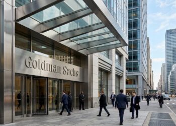 Entrada de la sede de Goldman Sachs en Nueva York, con el letrero corporativo sobre las puertas de cristal y personas con trajes caminando. Fotografía de prensa financiera.