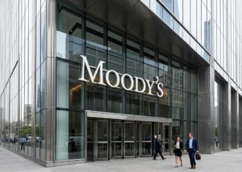 Entrada de rascacielos de cristal con el cartel de Moody's. Profesionales con traje caminan por la acera de enfrente.