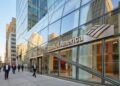 Entrada de la sede de Bank of America en NYC con el logotipo metálico en la fachada de vidrio, bajo la luz de la mañana.