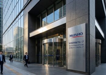 Entrada de Mizuho Financial Group en Tokio, con gran letrero metálico y hombres de negocios con trajes caminando por la acera.