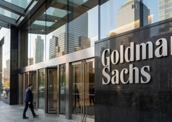 Entrada principal de Goldman Sachs con su nombre en granito oscuro y gente entrando por puertas de cristal en un entorno urbano.