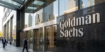 Entrada principal de Goldman Sachs con su nombre en granito oscuro y gente entrando por puertas de cristal en un entorno urbano.