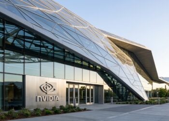 Entrada principal del edificio Voyager de NVIDIA con paneles de vidrio geométricos y un gran letrero de NVIDIA iluminado.