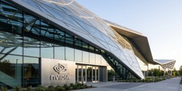 Entrada principal del edificio Voyager de NVIDIA con paneles de vidrio geométricos y un gran letrero de NVIDIA iluminado.