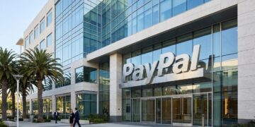Entrada principal moderna de la sede de PayPal con un gran cartel de la empresa, palmeras a la izquierda y dos hombres de negocios caminando por la acera.