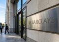 Entrada principal de Barclays con logo y nombre de la empresa grabados en una placa metálica en la pared de piedra.