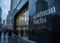 Empleados de negocios entran a la sede de Goldman Sachs en Nueva York, con el gran logo corporativo visible.