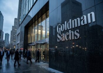 Empleados de negocios entran a la sede de Goldman Sachs en Nueva York, con el gran logo corporativo visible.