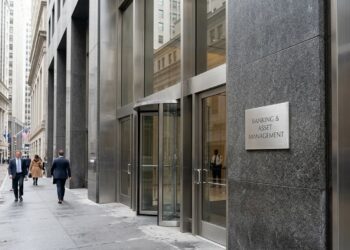Entrada de edificio moderno con puerta giratoria y placa de 'Banking & Asset Management'. Peatones caminan por la calle mojada.