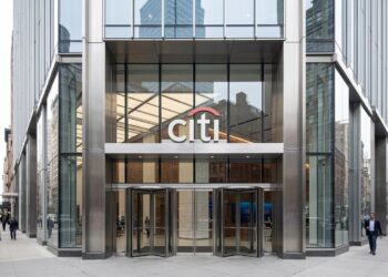 Entrada moderna de vidrio y acero con el logo "citi" en Nueva York. Peatones caminan por la acera y edificios urbanos al fondo.