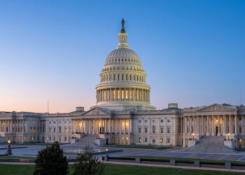 Vista exterior amplia del Capitolio de los Estados Unidos iluminado al crepúsculo. La cúpula y las alas son visibles bajo un cielo azul y naranja.