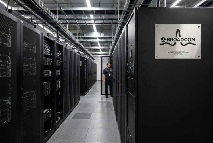 Un largo pasillo de servidores negros mate en un centro de datos de Google Cloud, con una placa de identificación de acero cepillado de Broadcom.