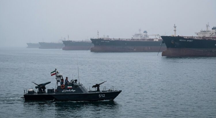 Lancha militar de Irán con bandera navega cerca de grandes buques petroleros en el mar brumoso de Hormuz.
