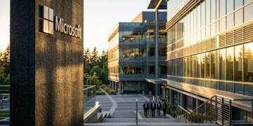 Cartel de Microsoft sobre pilar de piedra con edificios de oficinas y árboles al fondo.