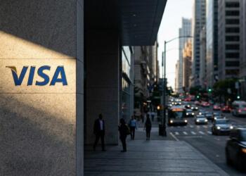Letrero de Visa en un pilar de piedra iluminado por el sol frente a una calle concurrida de la ciudad.