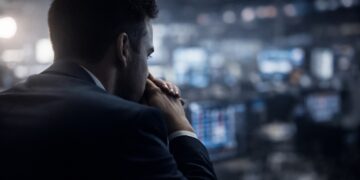 Trader en primer plano con fondo bursátil desenfocado y tenso.