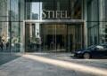 Fachada de vidrio de la oficina de Stifel con auto de lujo estacionado frente a la entrada.