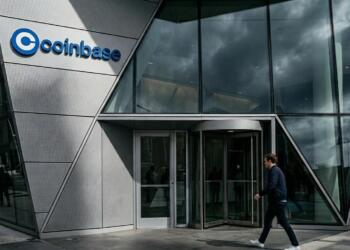 Entrada acristalada del edificio Coinbase con un hombre caminando por la acera.