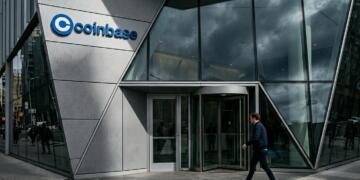 Entrada acristalada del edificio Coinbase con un hombre caminando por la acera.